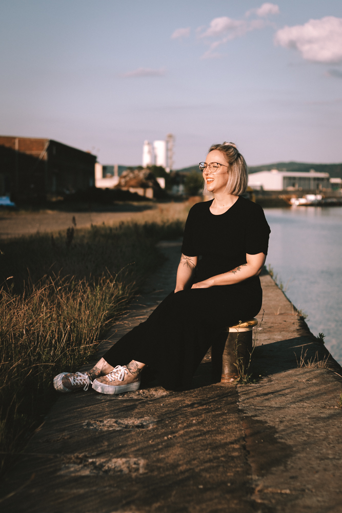 Portrait Shooting Hafen Aschaffenburg - Die schönste Frau sitzt lachend an einer Hafenmauer