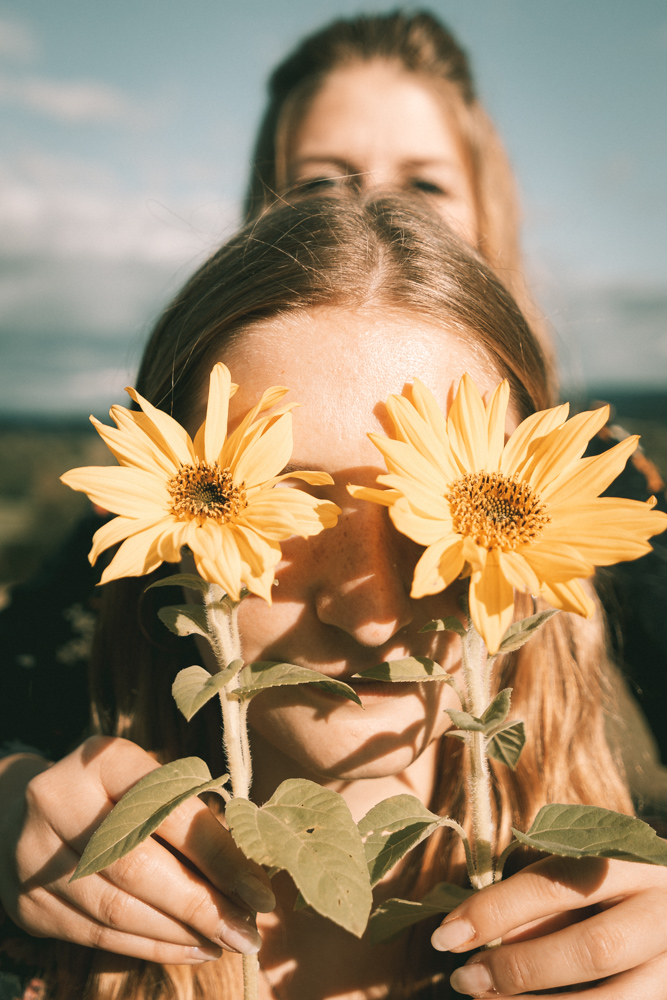 Schwestern Shooting - Eine Schwester hält der anderen Sonnenblumen vor das Gesicht